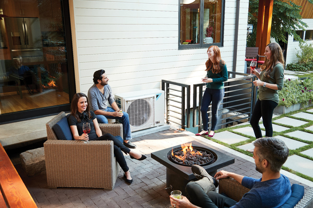 Group of people relaxing on an outdoor patio with a visible air conditioning unit nearby, enjoying comfortable temperatures
