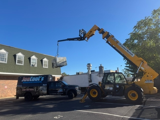 Construction equipment lifting a large HVAC unit from a truck outside a commercial building