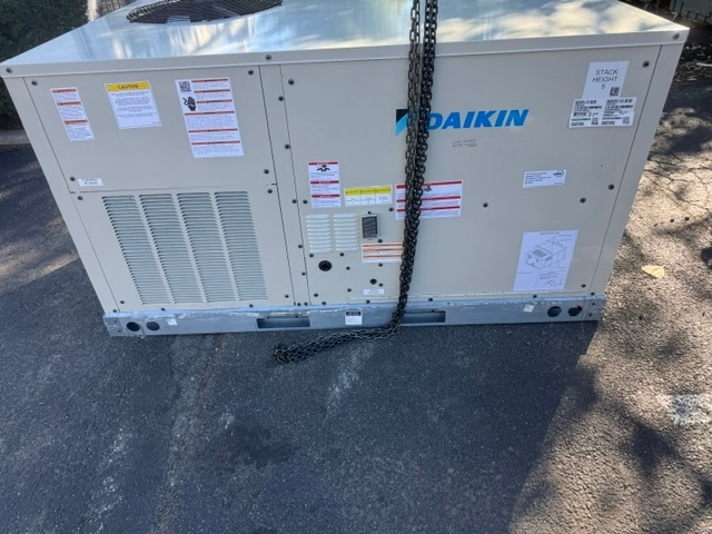 Large commercial HVAC unit secured with a chain, positioned on a paved surface prior to installation