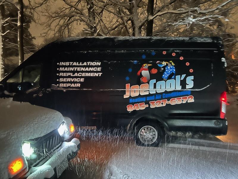 HVAC service van parked on a residential street during nighttime snowfall, responding to a winter service call.
